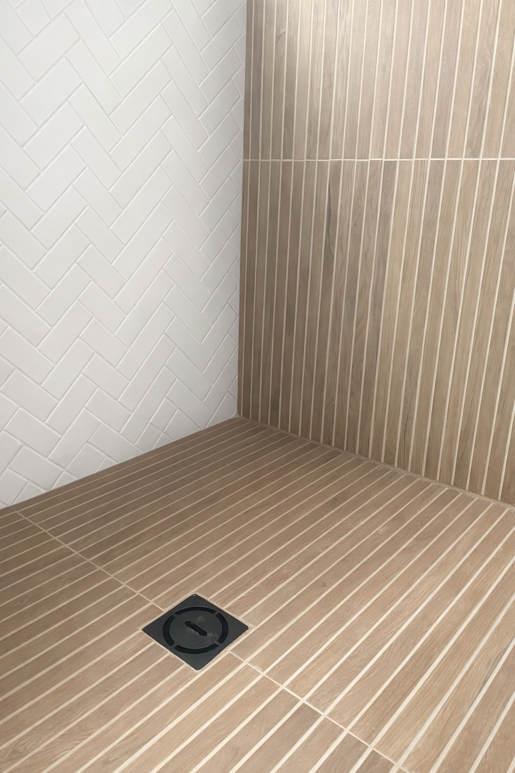 Close-up of a tiled bathroom shower with brown and dark blue tiles, a floor drain, and corner intersection of the walls and floor.