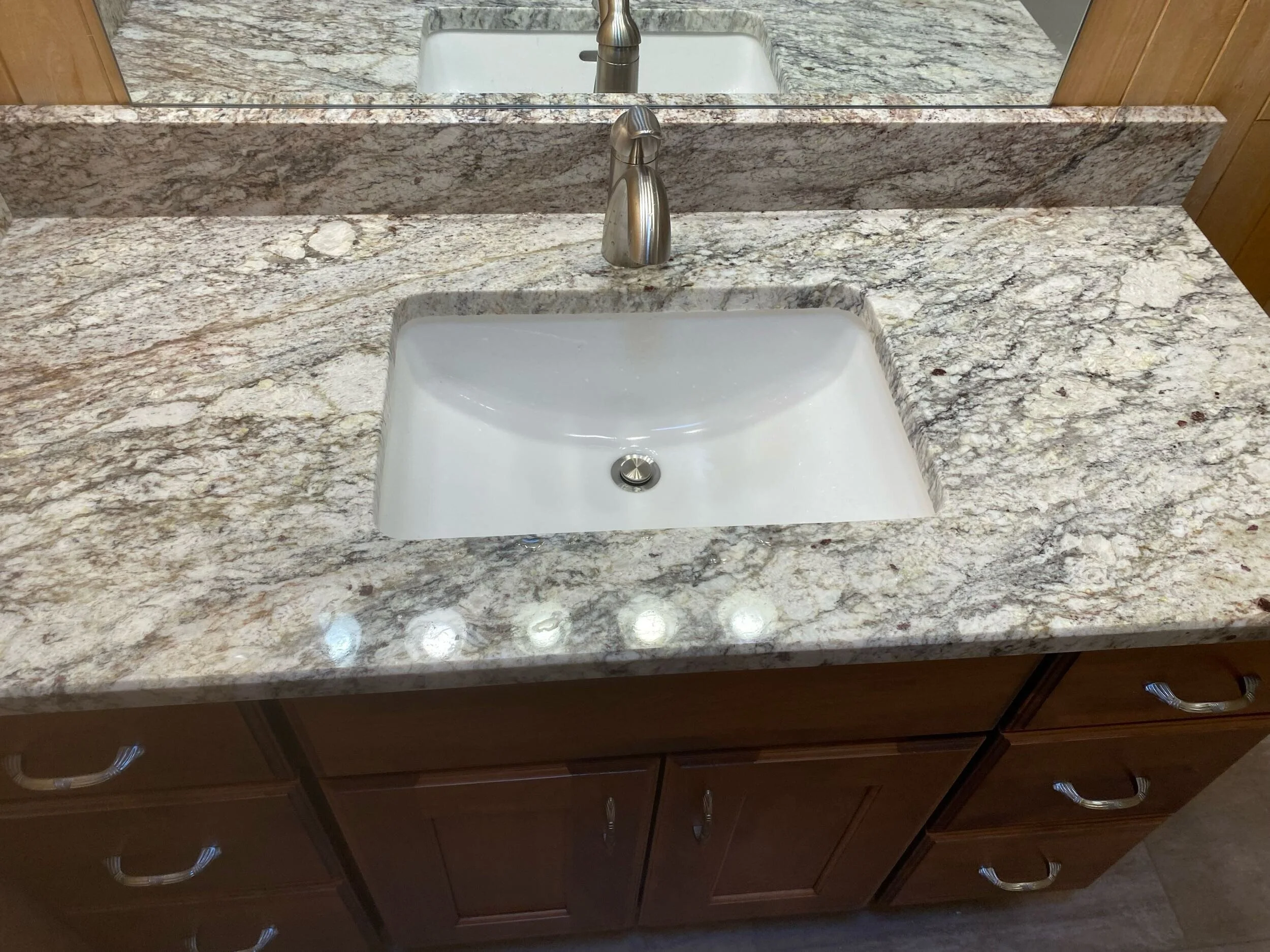 Bathroom vanity with a granite countertop, a white undermount sink, a brushed nickel faucet, and wooden cabinets below.