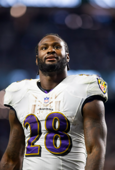 A football player wearing a Baltimore Ravens jersey with the number 28, standing on the field.
