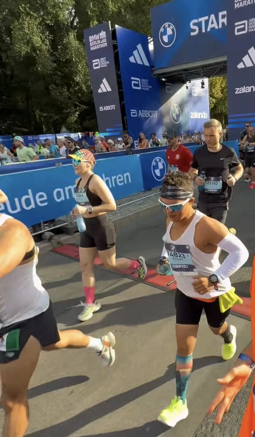 Marathon runners participating in the Berlin Marathon, with spectators and large sponsor banners in the background.