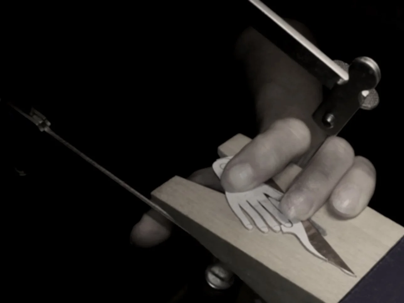 Person carving a hand shape into a piece of wood using a precision tool, with a dark background.