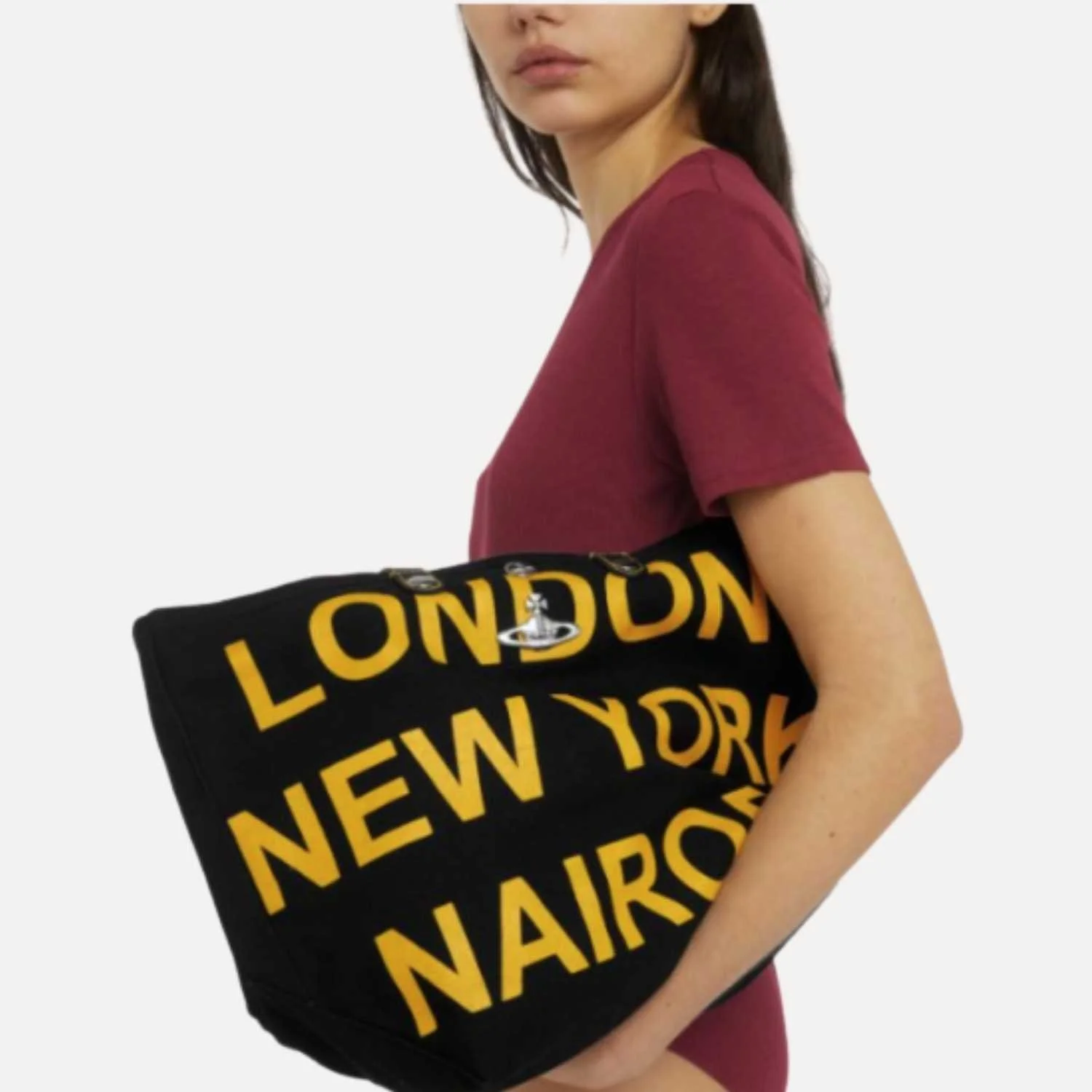 A woman in a maroon T-shirt holding a upcycled black duffle bag with yellow text manufactured by Beyond Remade for the Vivienne Westwood brand.
