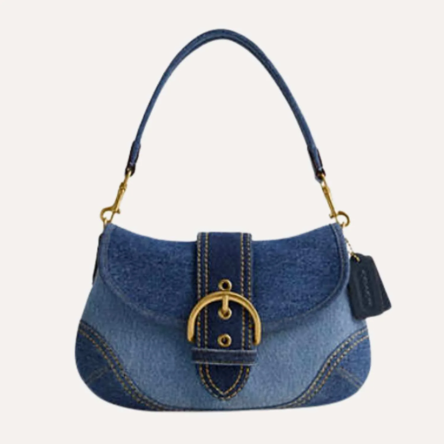 A handbag made from upcycled blue denim fabric with a gold buckle detail and a black tag attached on the side. Manufactured by Beyond Remade for the global fashion brand Coach.