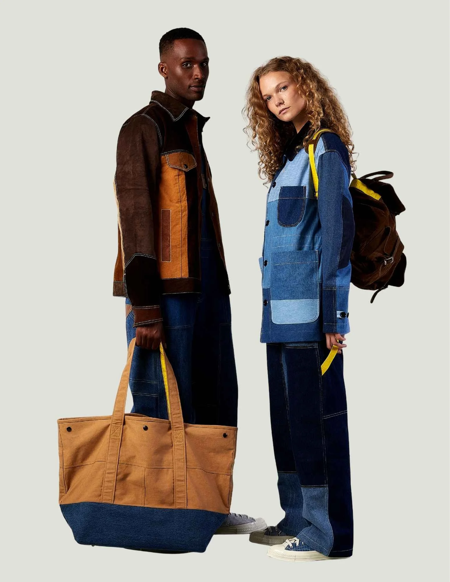 Two models standing side by side, holding large tote and backpack, wearing upcycled denim jackets and jeans from Beyond Remade.