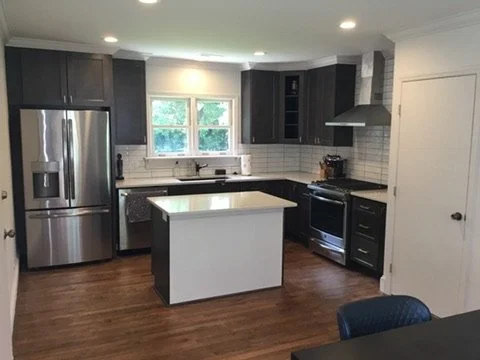 Modern kitchen with dark cabinets, stainless steel refrigerator, black stove, white backsplash, kitchen island, and hardwood floors.