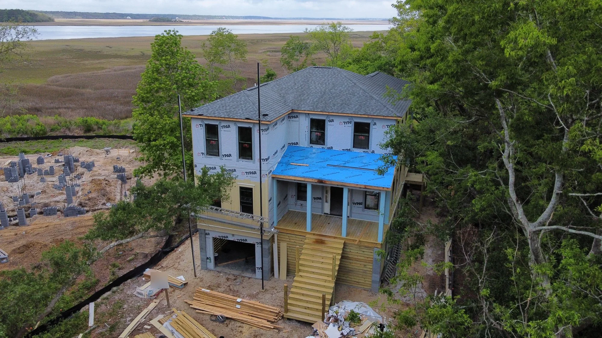 Aerial view of a marsh-side new build with a finished shingle roof and porch roof underlayment