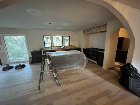 Living room under renovation with plastic-covered furniture, a step ladder, and construction materials