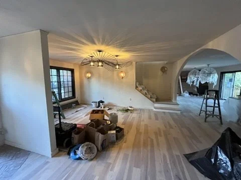 Living room under renovation with scattered items, a staircase, and a large window.