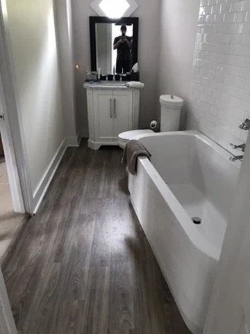 Bathroom with a bathtub, white tiled wall, wooden floor, mirror, and vanity with a sink