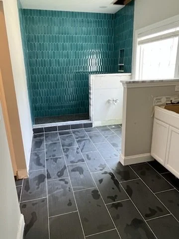 Bathroom with dark gray tiled floor, water stains, bright turquoise tiled wall, and a white shower or bathtub area.