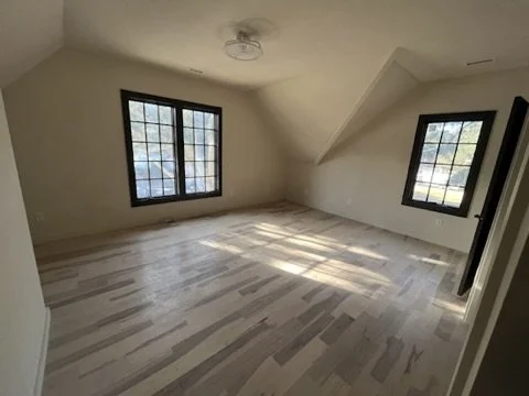 Empty room with two large windows, light-colored wooden floor, and sloped ceiling in an attic space.
