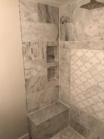 Inside a marble-tiled shower with built-in shelf and a bench.