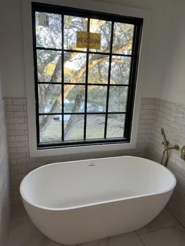 Empty bathtub in a bathroom with a large window showing trees outside.