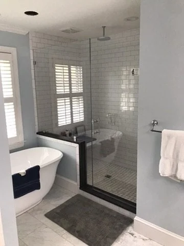 Bathroom with a freestanding bathtub, a glass-enclosed shower with white subway tiles, a small window with shutters, and a towel hanging on a rack.