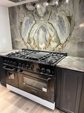 Black stove and oven with marble countertops in a kitchen with a large rock wall featuring a natural fossil or mineral formation