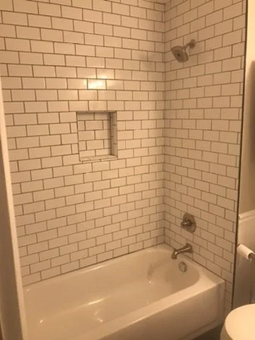 Bathroom with white subway tile and a built-in shower niche, bathtub, and shower fixtures.