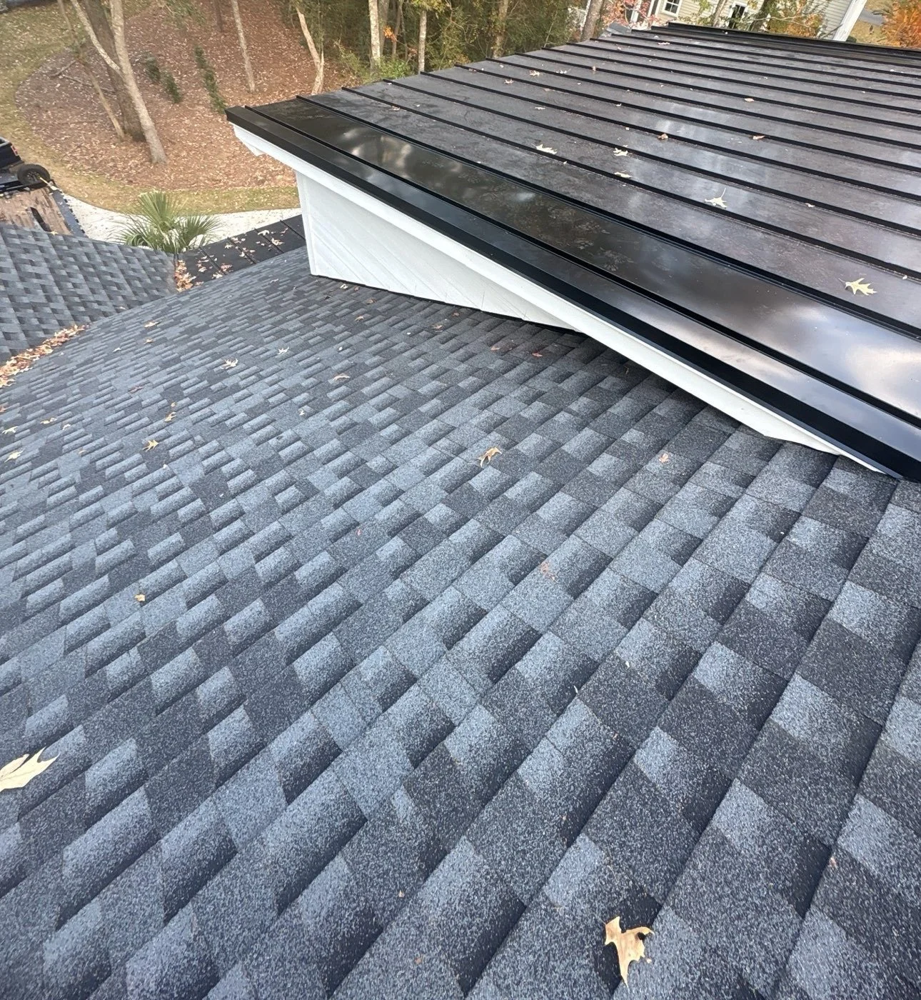 Architectural shingles tied into a black standing-seam metal roof section