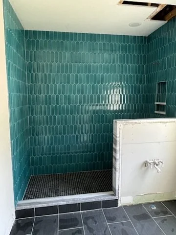 Empty shower area with teal tiles on the walls, black tiny tiles on the floor, and a missing ceiling panel showing water damage.