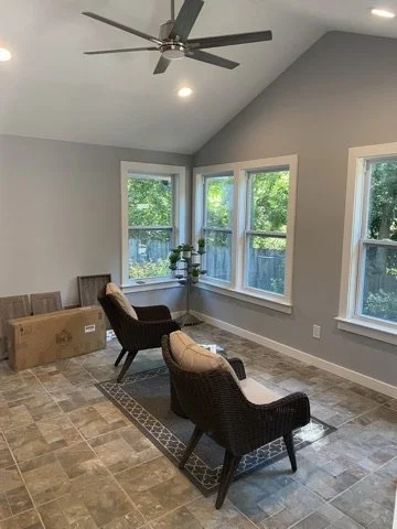 Living room with three chairs, a small table with plants, large windows, recessed ceiling lights, and a ceiling fan.