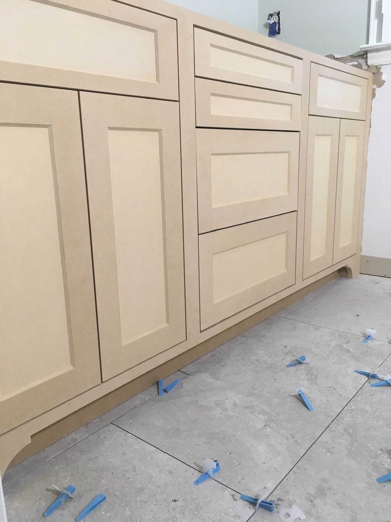Kitchen cabinets under construction with a white wall, electrical outlets, and tools on the floor.