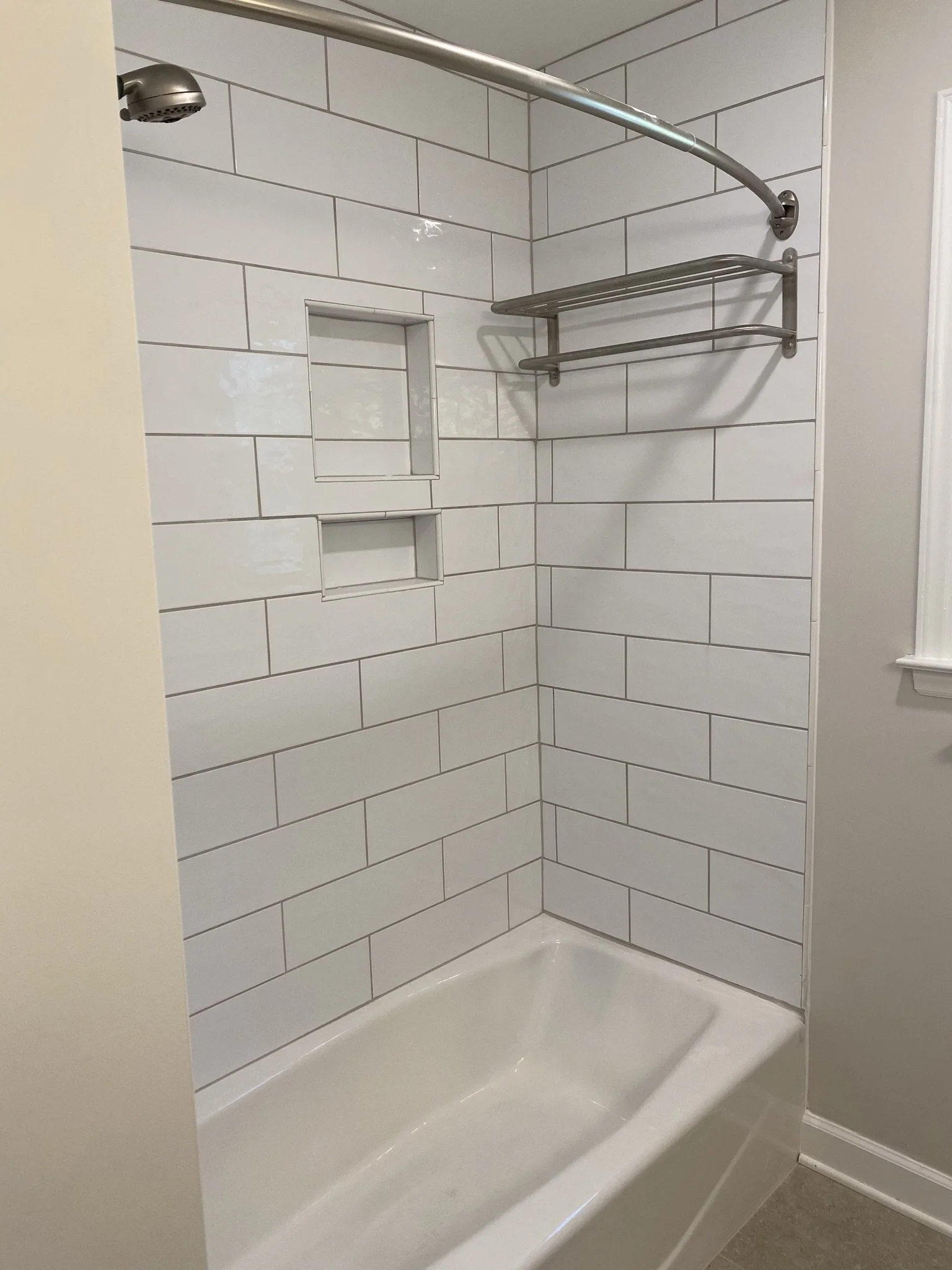 A corner shower with white subway tile walls, built-in wall niches, a stainless steel shower rod, and a white shower base.