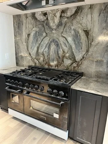 A modern kitchen with a black stove and oven, gray cabinets, and a marble backsplash with a natural stone pattern.