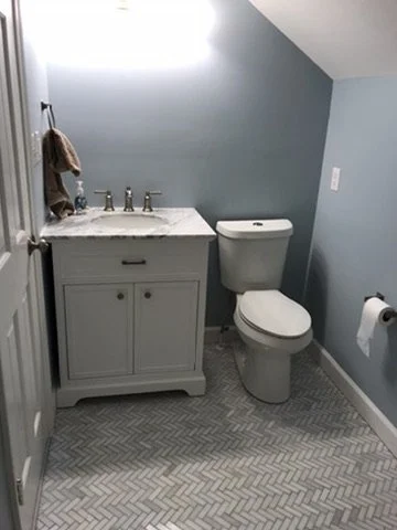 Small bathroom with blue walls, white vanity with marble top, toilet, and a toilet paper holder on the wall.