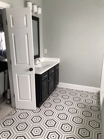 Bathroom with a black vanity, white countertop, gray walls, and a patterned hexagon floor tile.