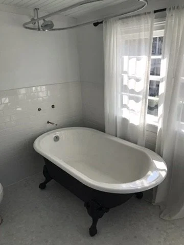 Empty bathroom with a vintage clawfoot bathtub next to a window with sheer curtains.