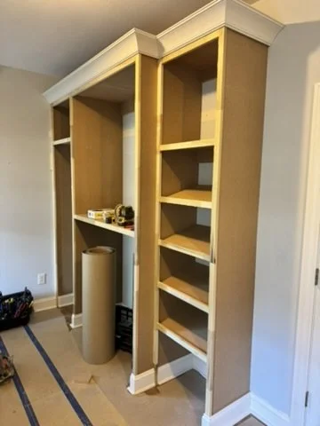 Empty built-in wooden shelves and cabinets in a room under renovation.