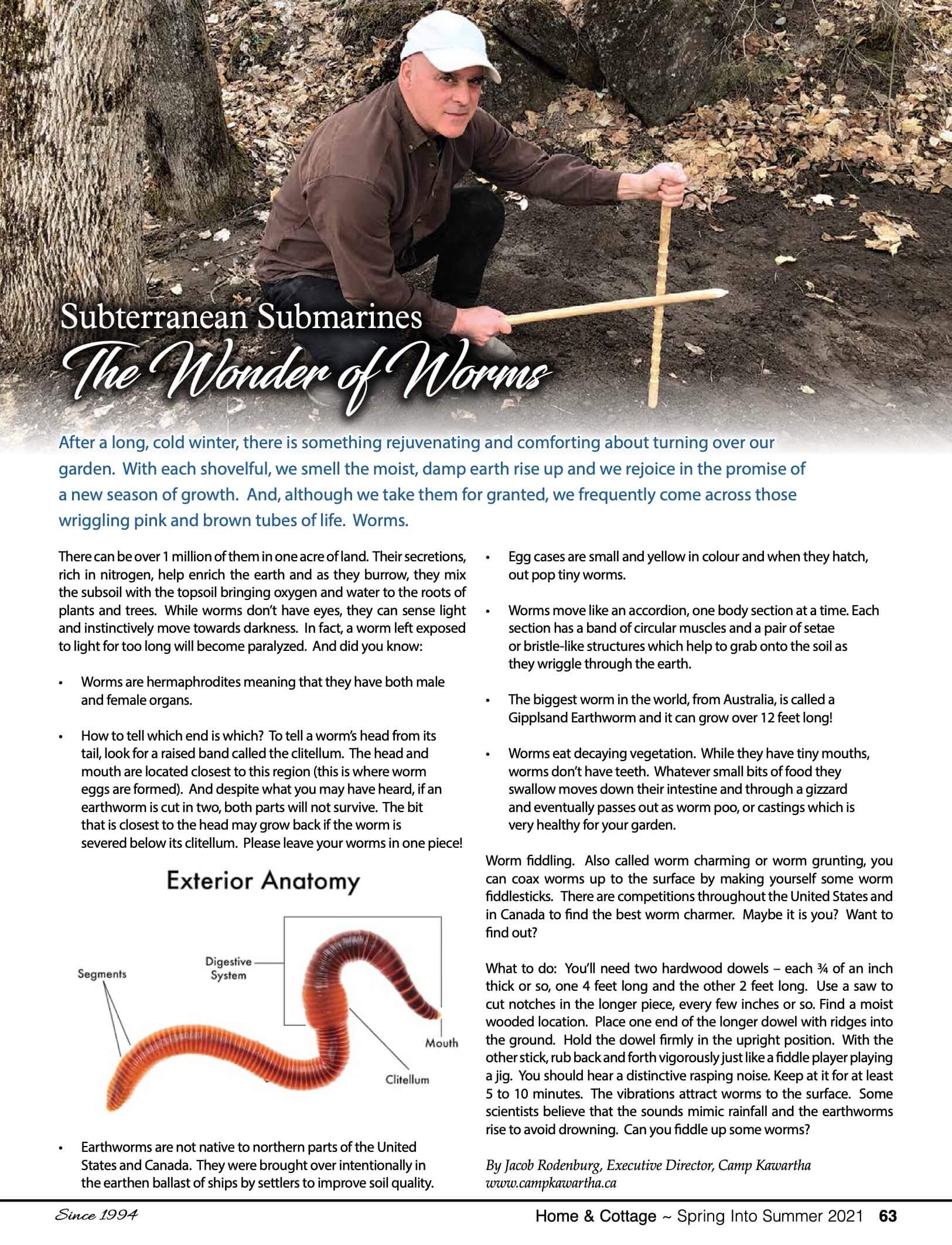 A man crouching outdoors next to a large tree, using a measuring stick to examine a patch of earth. The scene includes fallen leaves and a rocky background, with an article titled 'The Wonder of Worms' discussing subterranean worms, their anatomy, and their role in soil health.