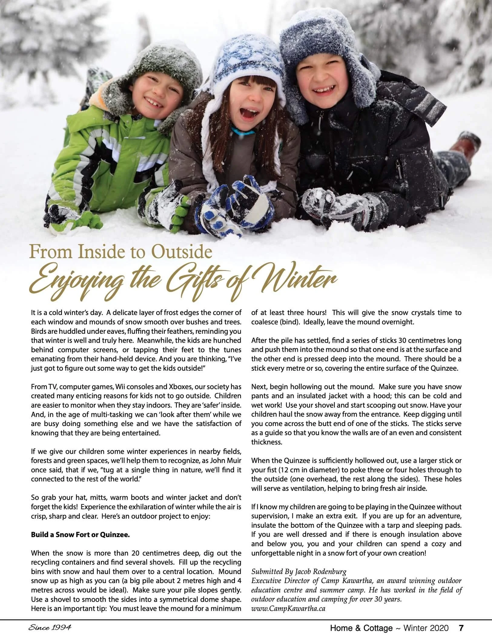 Photo of three children lying on snow in winter, smiling and wearing winter clothing including hats, jackets, and gloves.