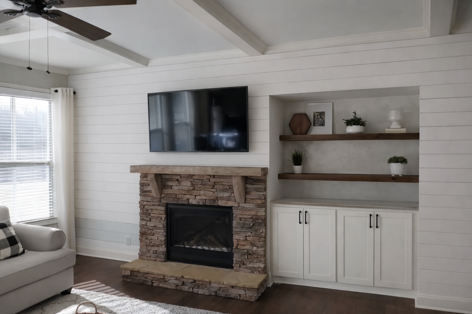 Interior renovation showcasing a stone fireplace with wood mantel, mounted television, custom cabinetry and open shelving, completed by Wilken Precision Remodeling.