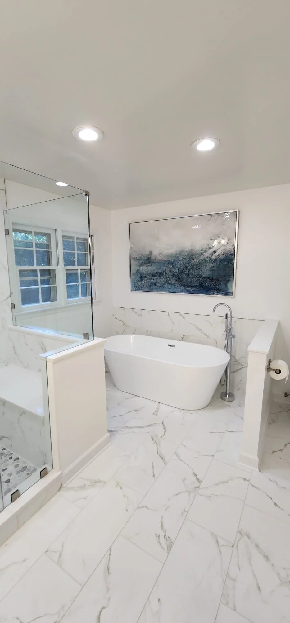 Modern bathroom remodel with freestanding soaking tub, marble tile flooring and wall accents, glass- enclosed shower, and natural light designed by Wilken Precision Remodeling.
