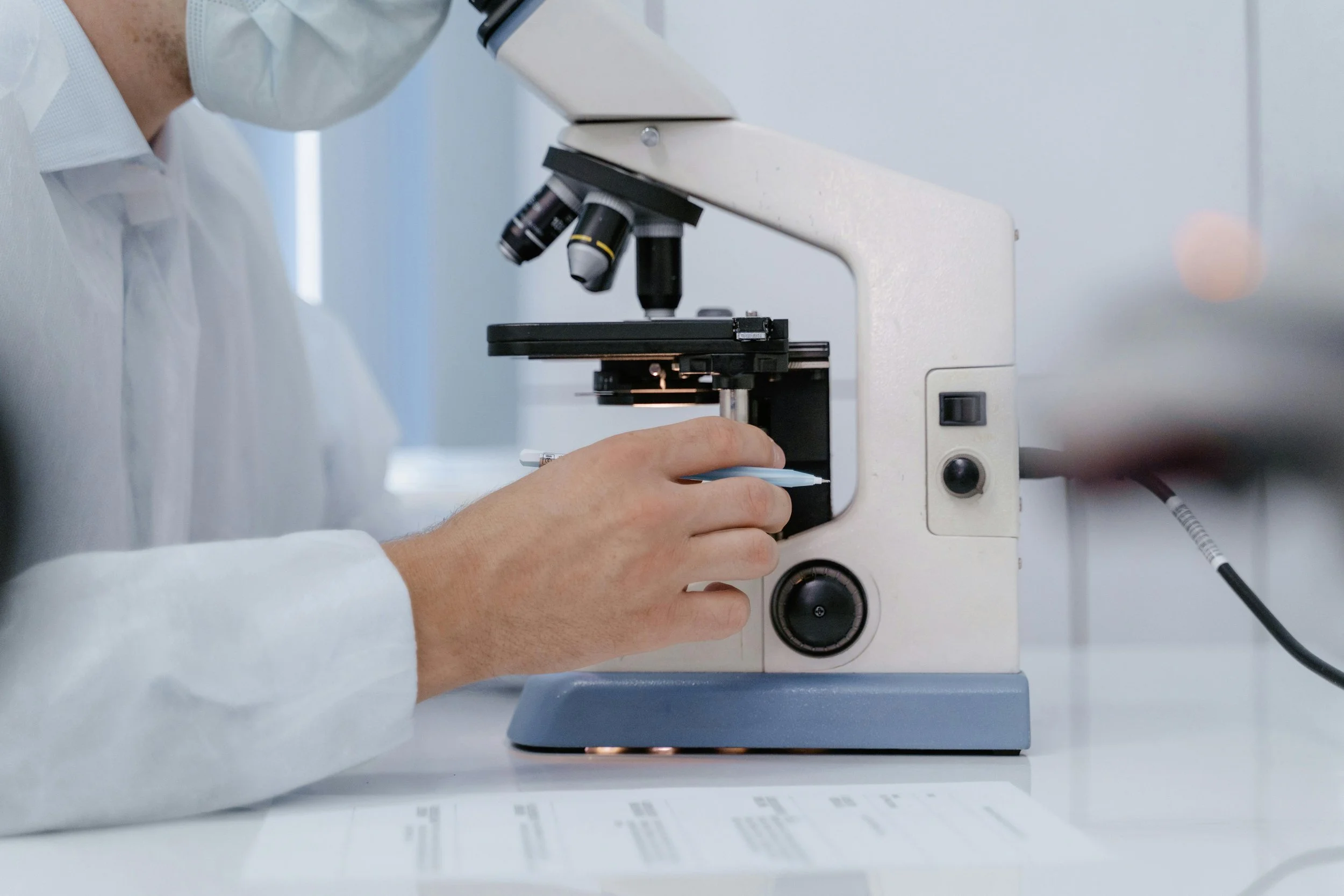 Close-up shot of person wearing surgical mask and lab coat, gazing into microscope