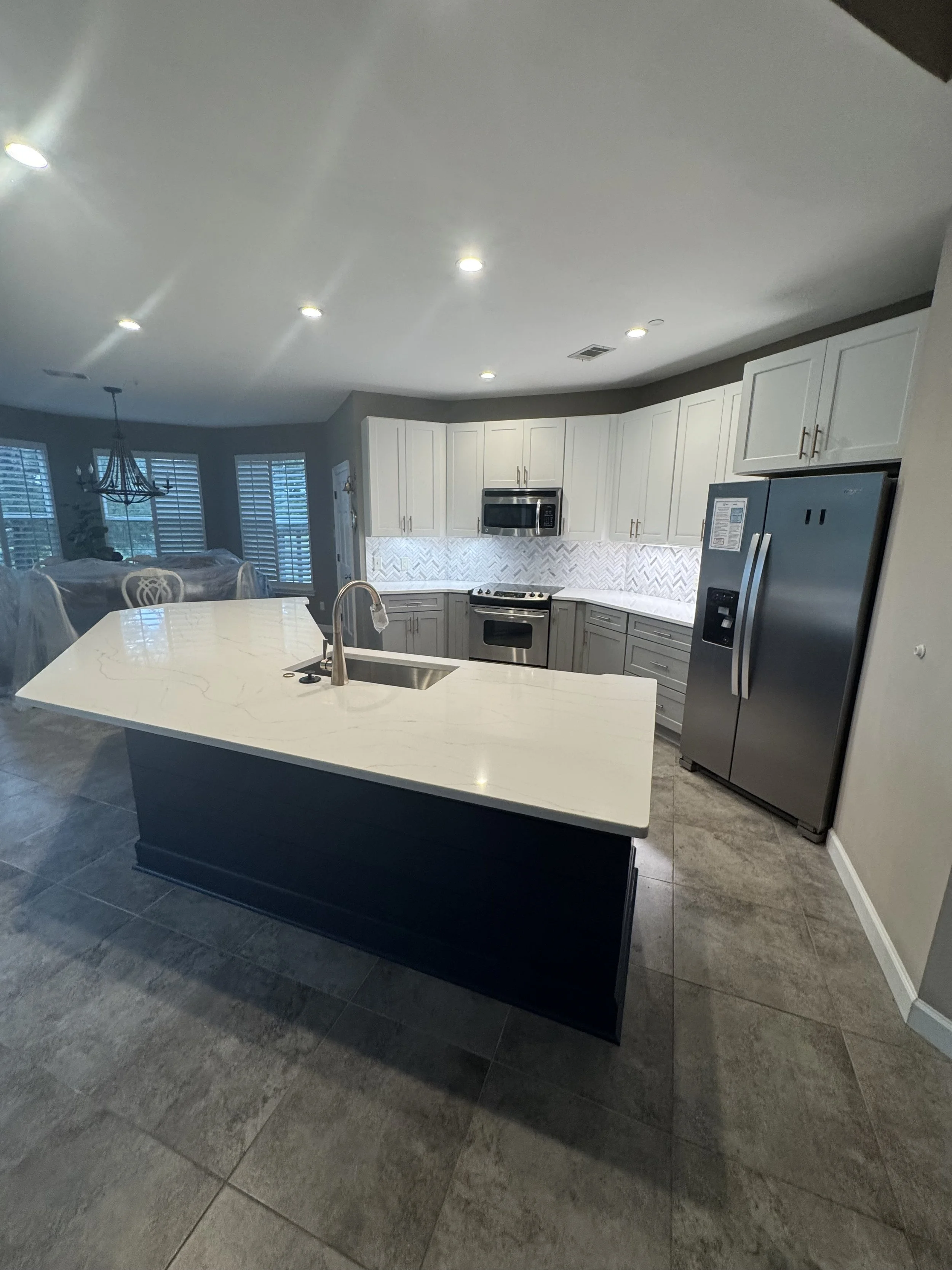 Modern kitchen with white cabinets, stainless steel refrigerator, black stove, microwave, and an island with a sink, in a home with tiled flooring.
