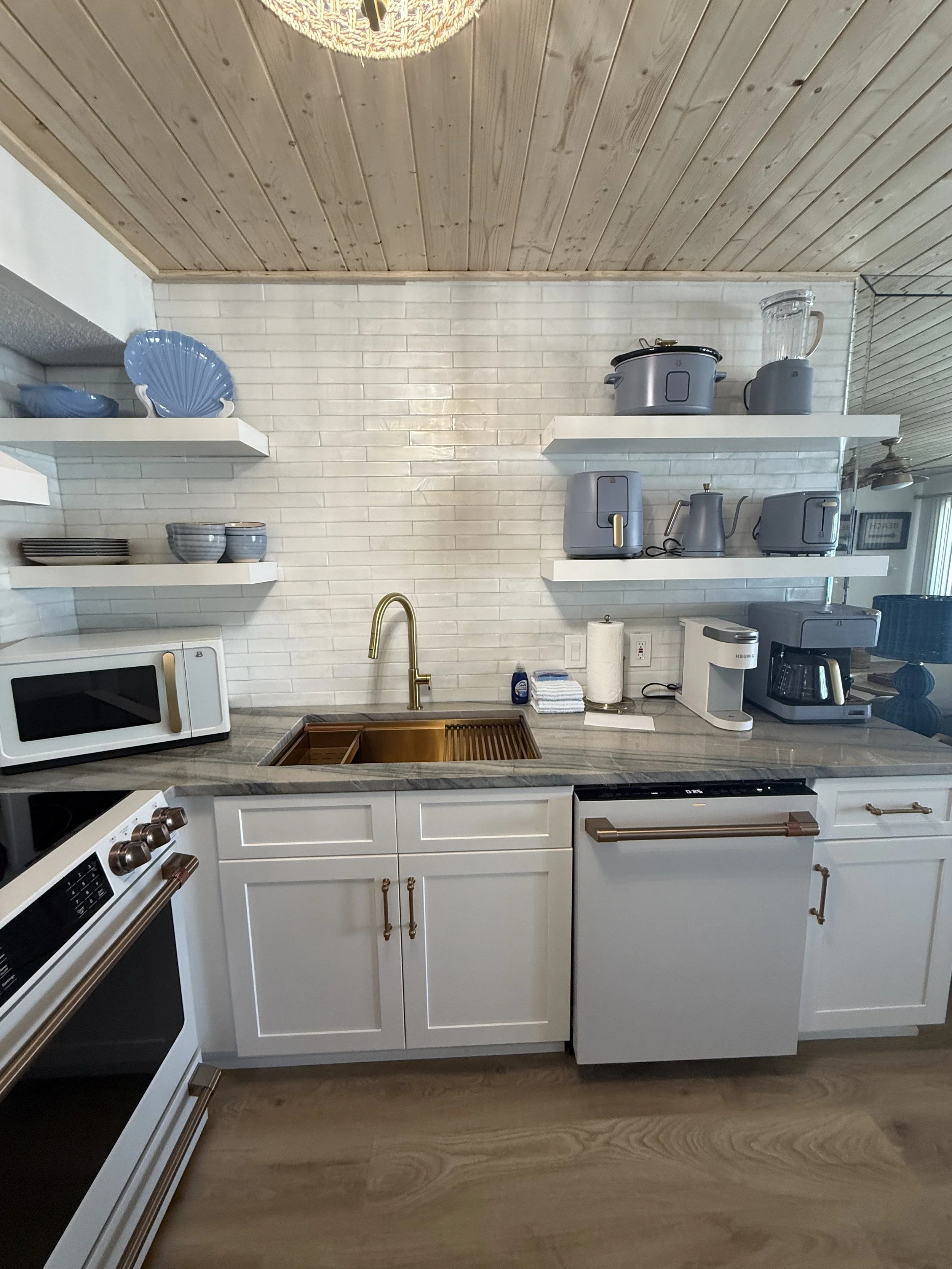 A modern kitchen with white cabinets, a gold faucet, and white open shelves holding blue dishes and kitchen appliances.
