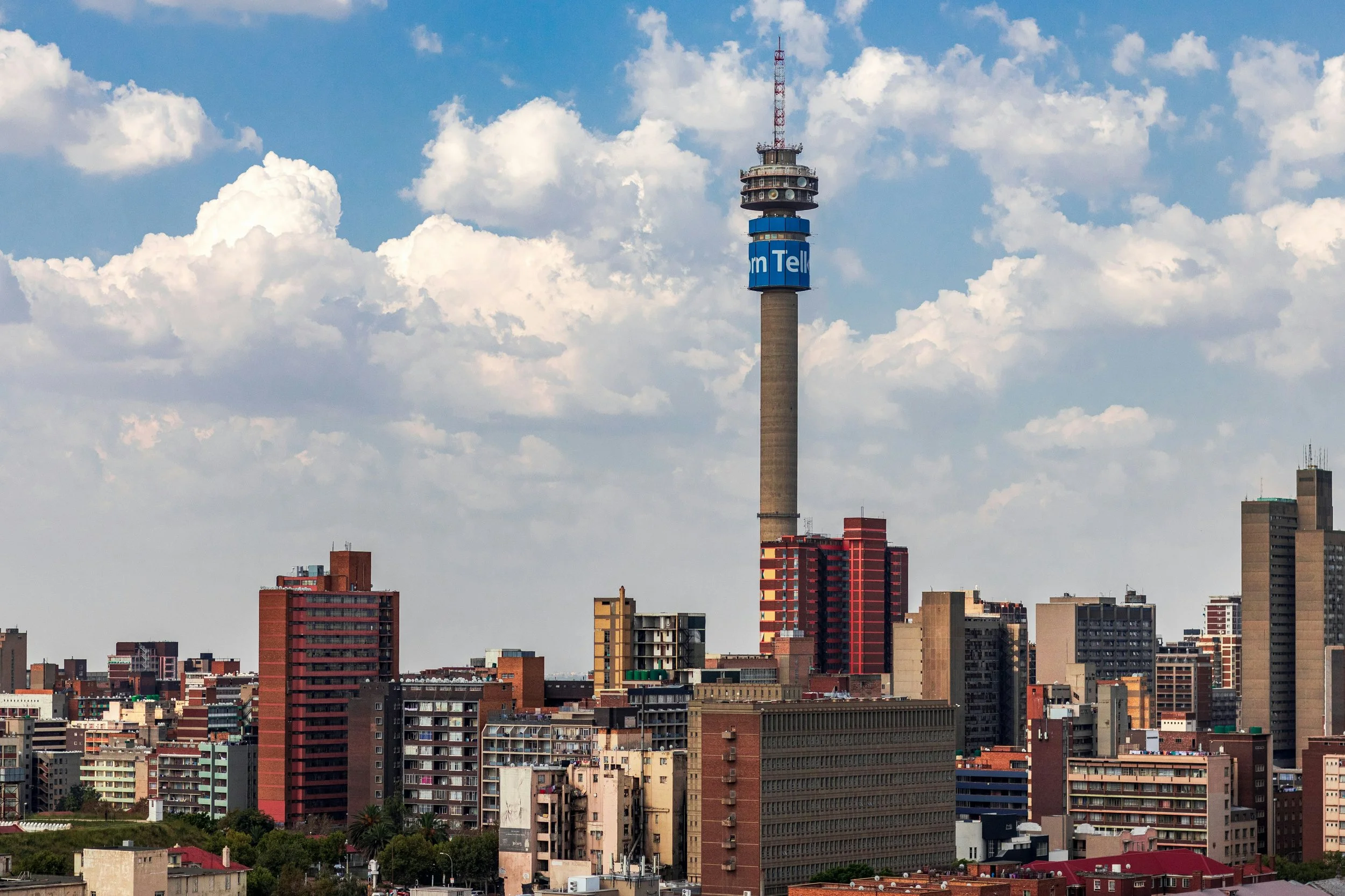 City skyline with a prominent tall television tower, partly cloudy sky.