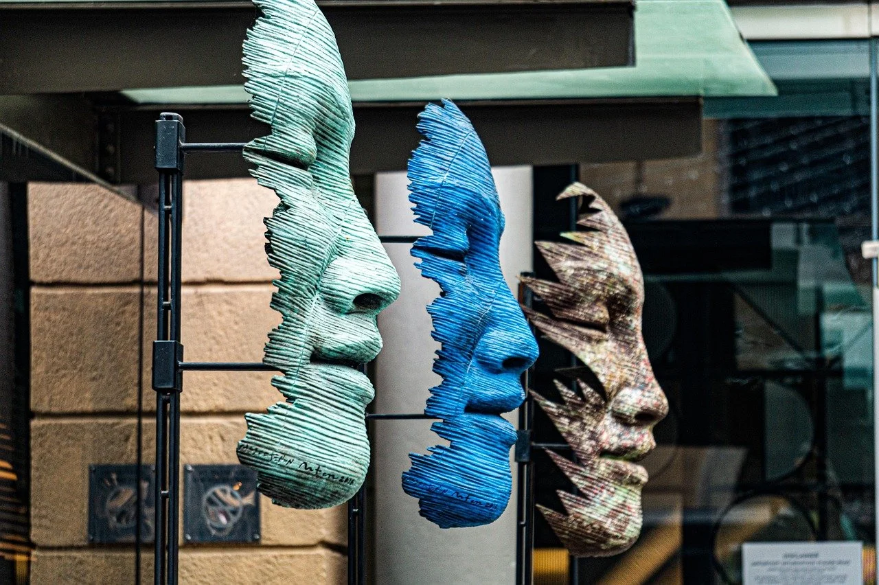 Three colorful sculptures of human faces in profile, displayed outdoors on black stands