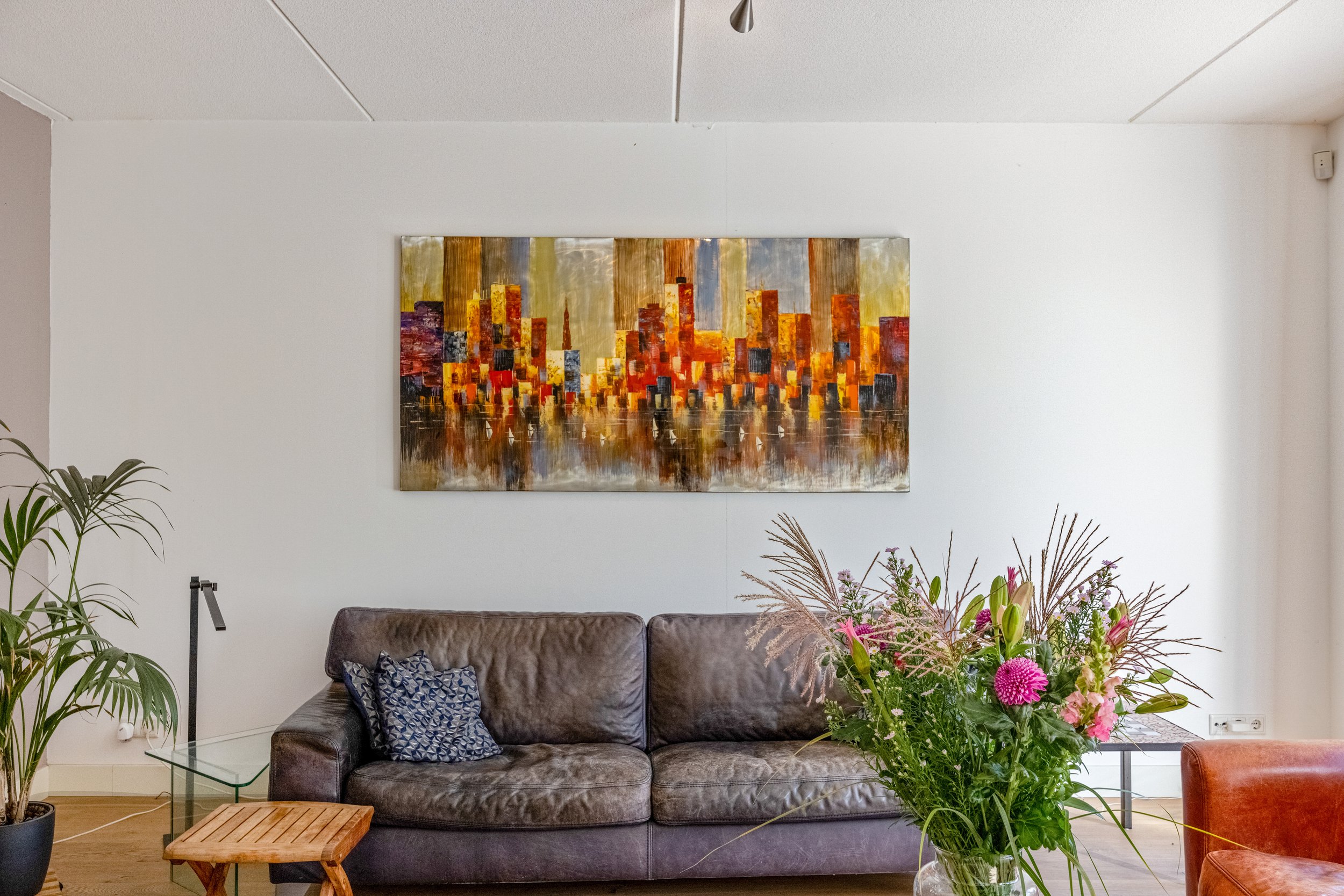 Woonkamer met bank, bloemen en abstract stadsgezicht schilderij