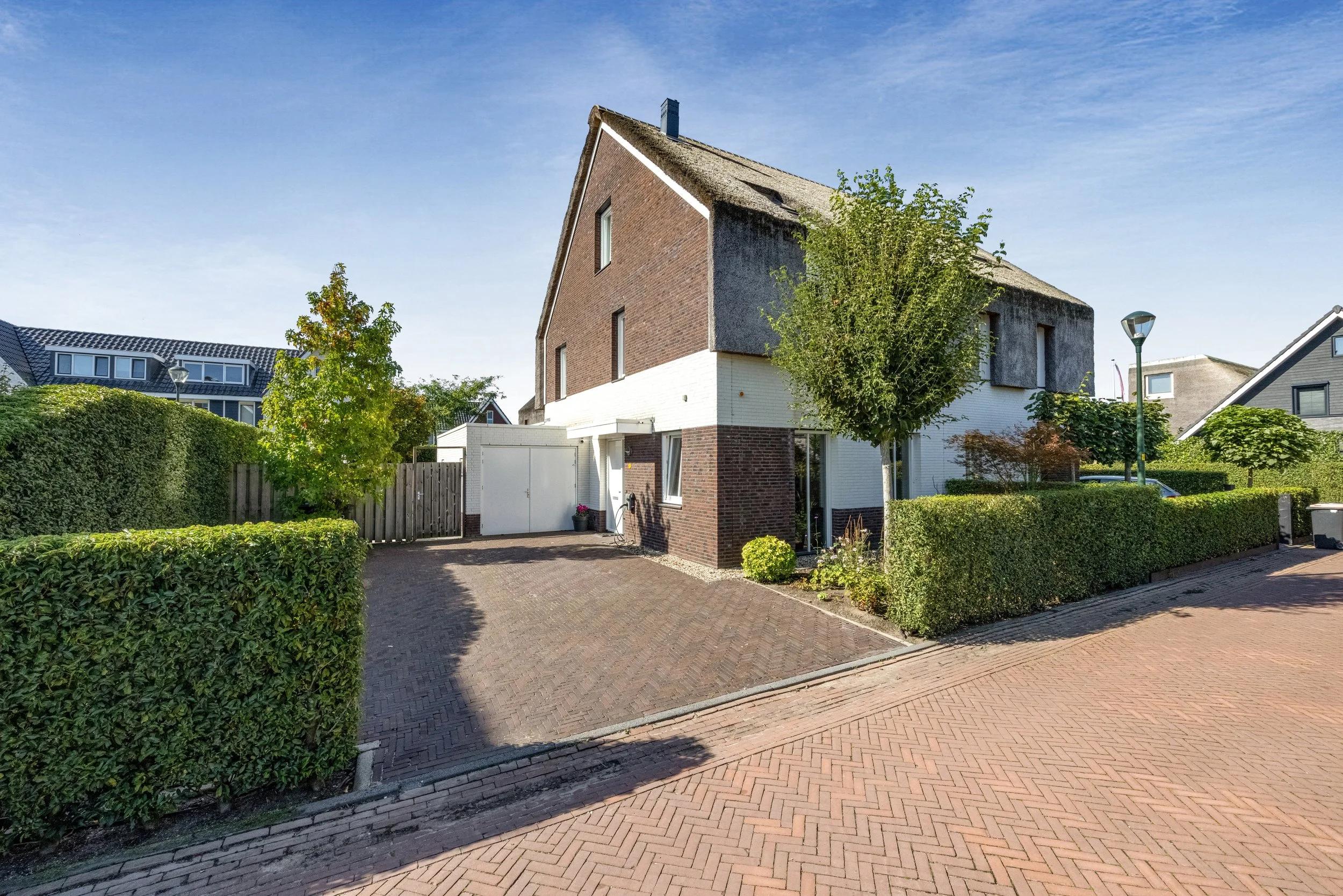 Gezicht op een moderne tweekapper met een tuin, oprit en een witte garage, in een rustige woonwijk onder een heldere blauwe hemel.