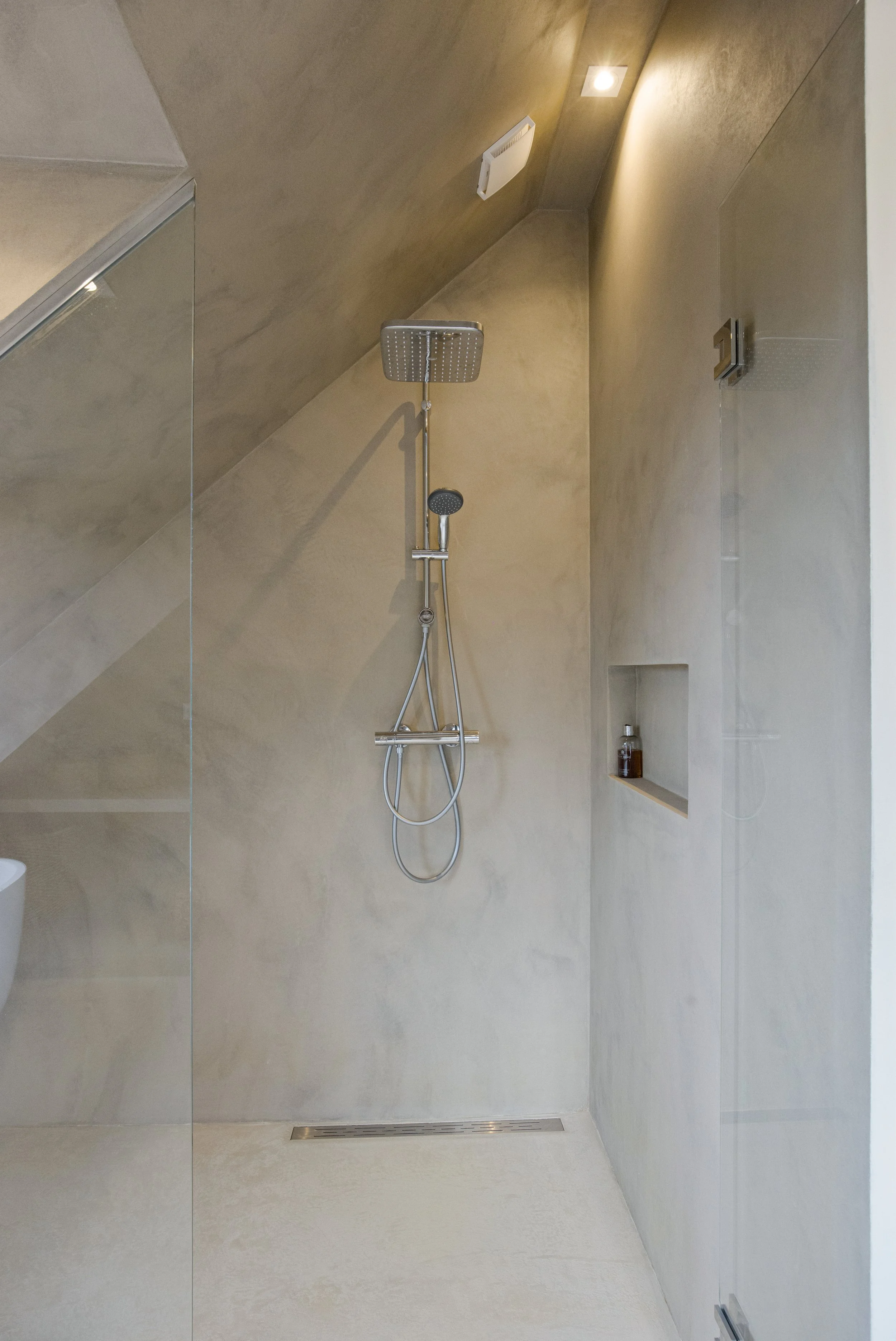 Moderne inloopdouche met een regen(douche)kop en een handdouche, ingebouwde nis met zeep en shampoo, en een afvoer in de vloer