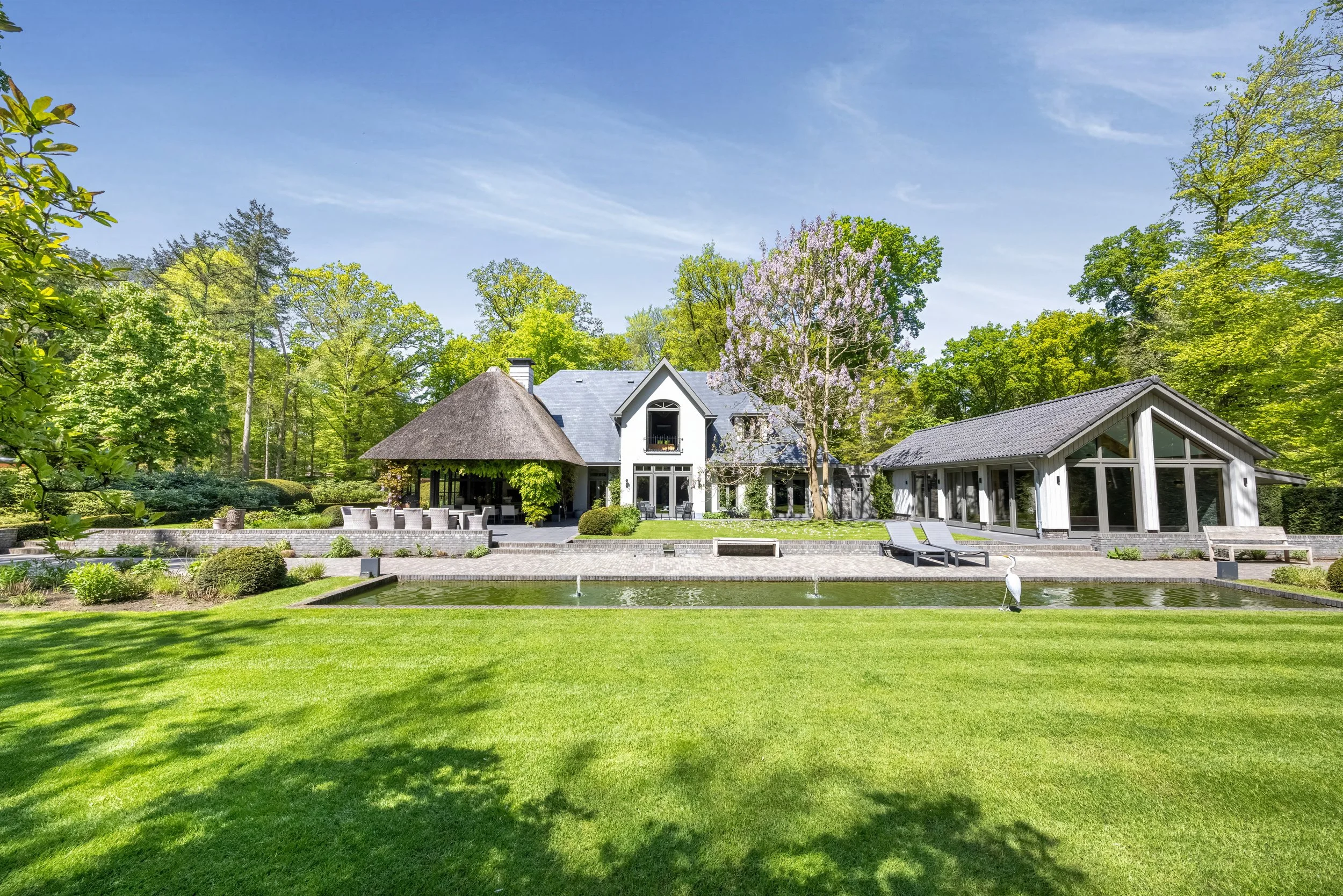 Luxe herenhuis met veranda, tuin en opppervlakte met water, omgeven door bomen.