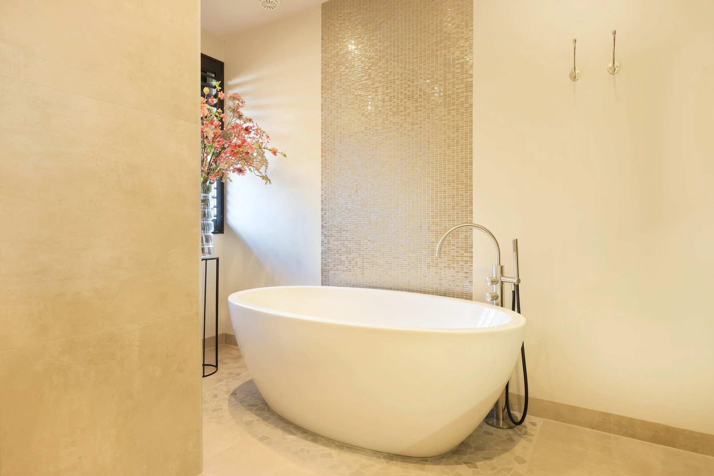 Moderne badkamer met free-standing bad, roze bloemen in een vaas, en natuurlijke tinten