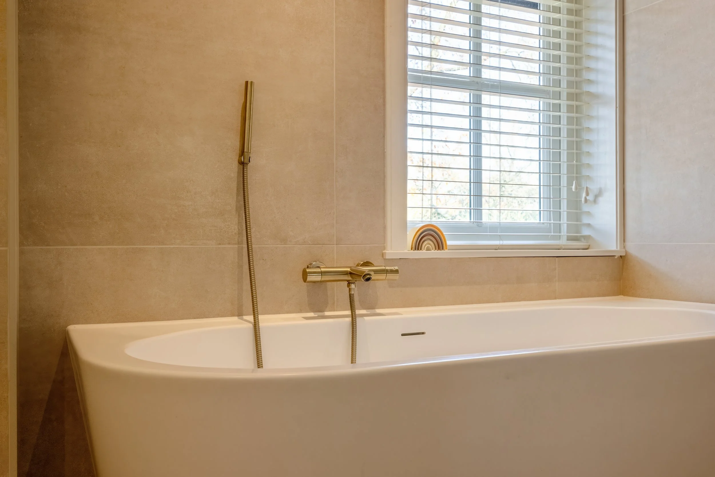 Moderne badkamer met een wit bad, een raam met witte jaloezieën, en een geel/oranje decoratief item op de vensterbank.