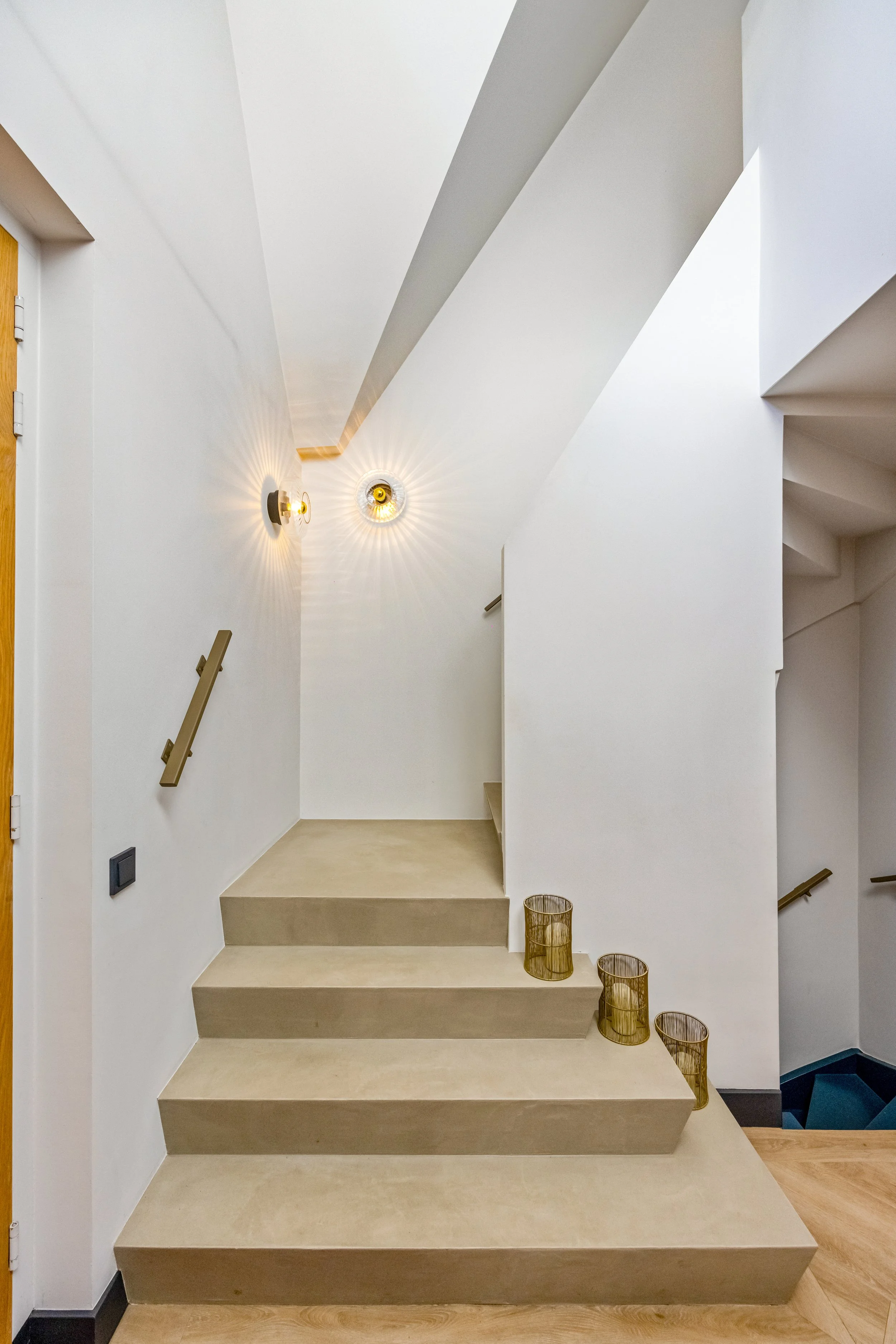 Moderne binnenhuisarchitectuur met witte muren, beige trap, muurbeugel, wandlampen en gouden decoratieve sierpotten.