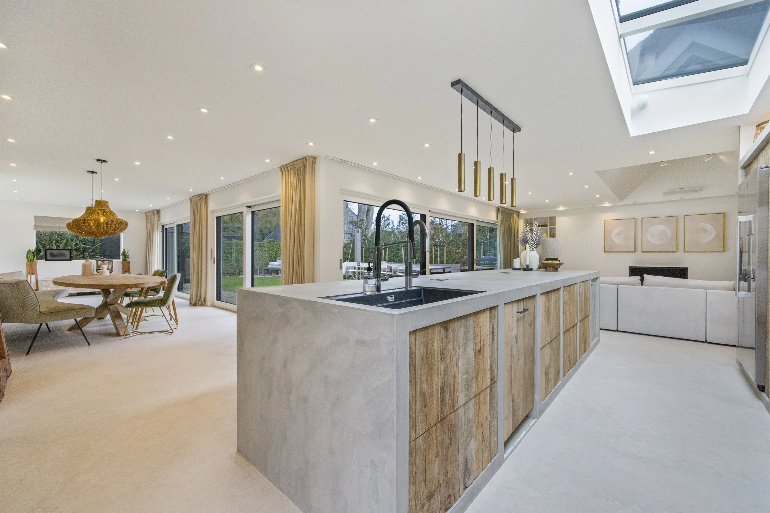 Moderne open keuken met een eiland, groot raam, eettafel en zithoek in een lichte woonkamer