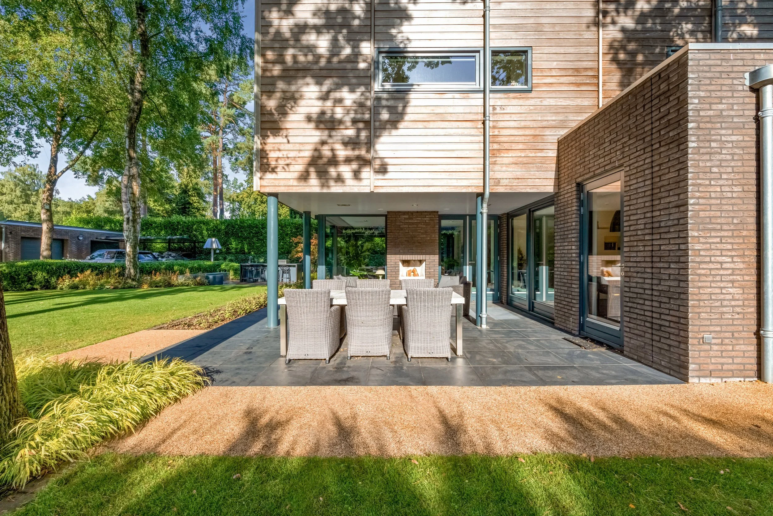 Moderne woning met tuin en terras, rijk aangelegd met gras, bomen en planten, buitenkeuken en tuinset.