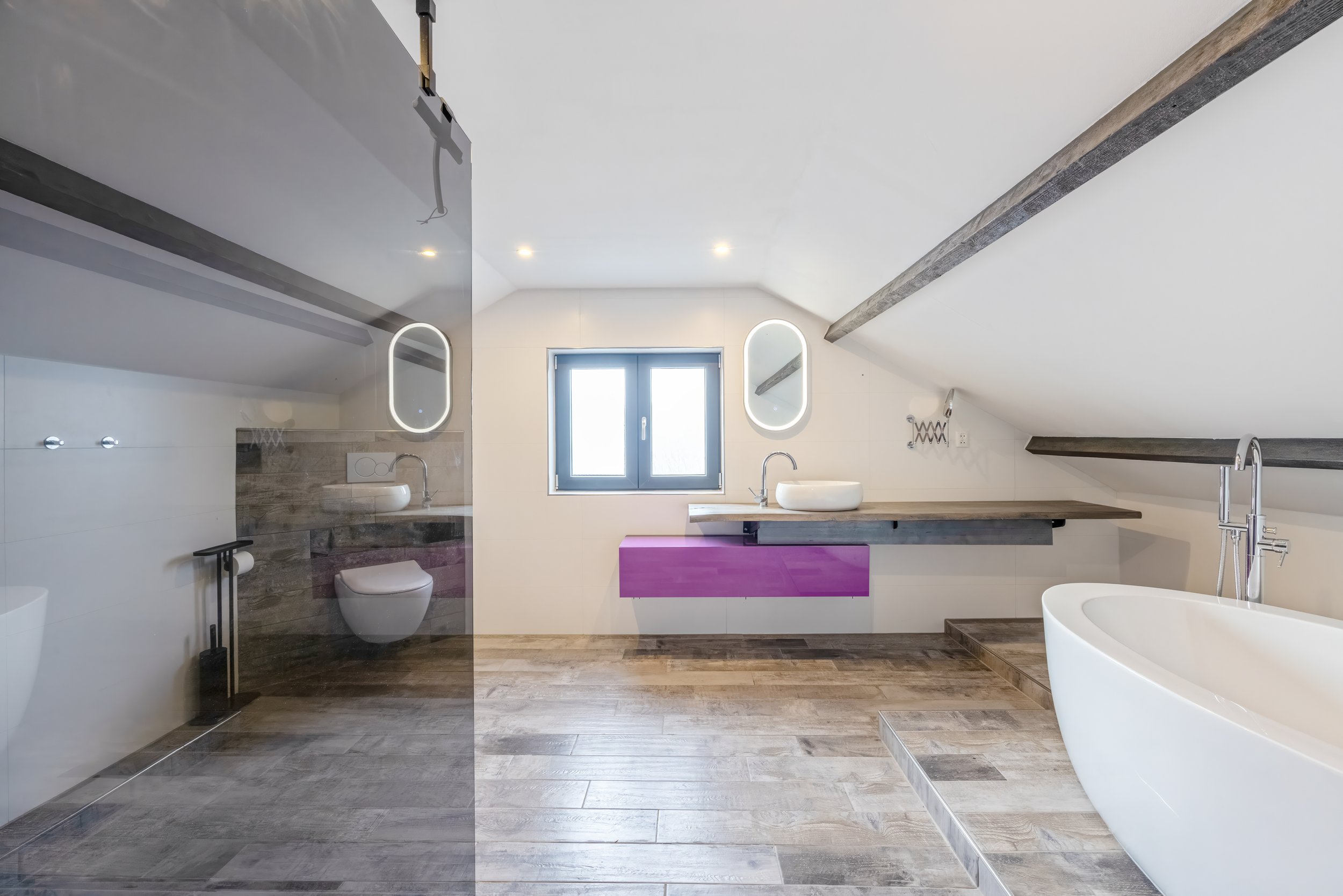 Een badkamer met een douchecabine, een hangend toilet, een wastafel met spiegel, een ligbad, houten vloer en plafondbalken.