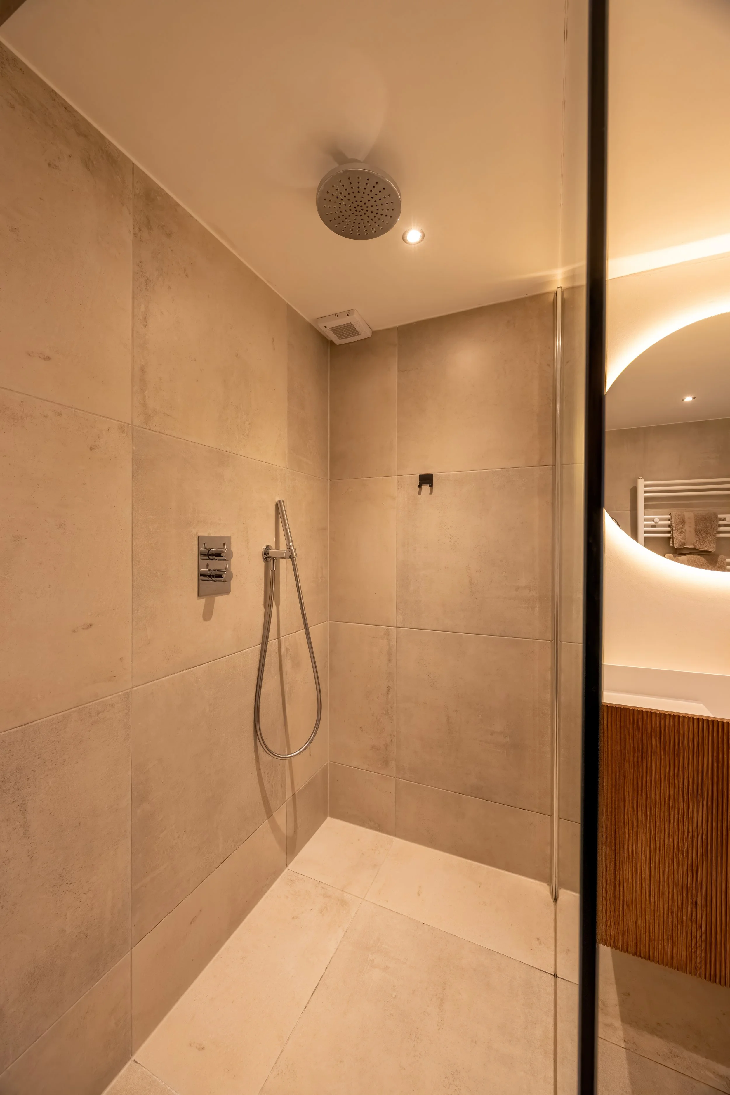 Lege inloopdouche met beige tegels, regen-douchekop en spiegel die reflecteert wat in de badkamer te zien is.